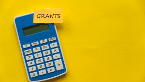 Image of a calculator & the words "Grants" written on a sticky note, attached to the calculator