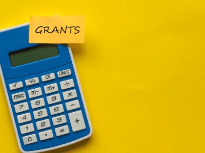 Image of a calculator & the words "Grants" written on a sticky note, attached to the calculator